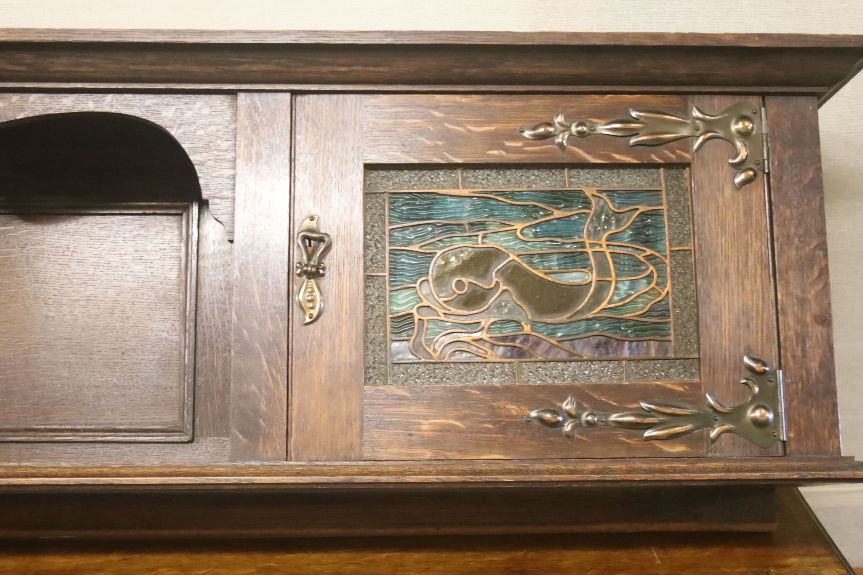 An Arts & Crafts style oak sideboard with stained glass dolphin panels, length 182cm, depth 60cm, height 145cm (lacks top section suppo